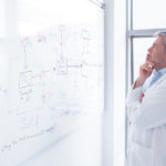 scientist in labcoat looking puzzled at whiteboard