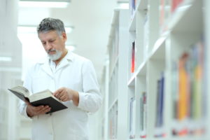 male scientist in white lab coat in library reading book