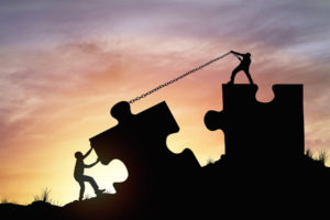 Silhouette of two people pulling giant-size jigsaw puzzle pieces together with chains, to visualise the concept of people working together to end the reign of the journal impact factor